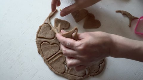 A female Baker prepares cookies. She cuts out a heart-shaped figurine from rolled brown dough on a white table. Close-up, high detail. The view from the top. 4K. 25 fps.