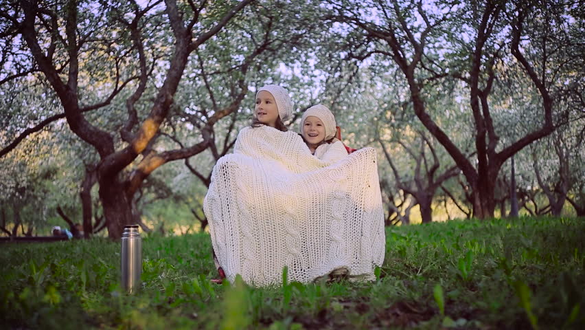 Two sisters sheltered by a plaid sitting in the park