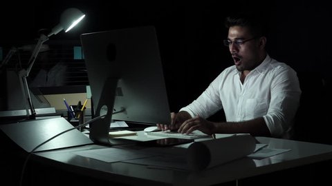 Workaholic Asian businessman working on computer late at night in the office feeling tired, sleepy and having neck pain from overwork
