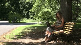 young student girl work with laptop sitting on wooden bench in green summer park outdoor. 4K UHD video clip.