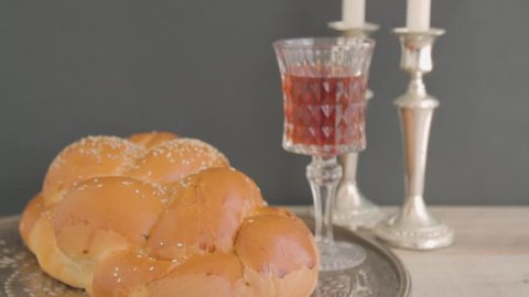 Shabbat or Sabbath kiddush ceremony composition with a traditional sweet fresh loaf of challah bread, glass of red kosher wine and candles on a vintage wood background. Tilt camera action