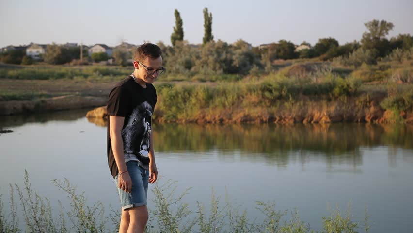 young boy throws a weed into water, lake