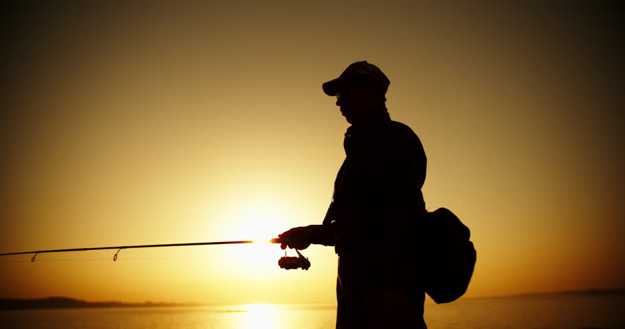 An experienced Fishman catching fish with professional spinning rod from a lake shore. lake in orange sunset 4k