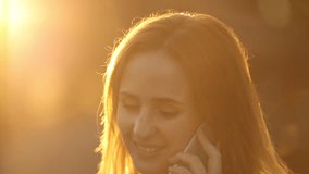 Portrait of beautiful red-haired girl with make up talking to a friend over cell phone. She is smiling and enjoying the call. Bright sunny background. 