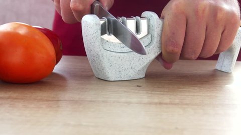 Manual sharpening of a knife in a special sharpener in a kitchen