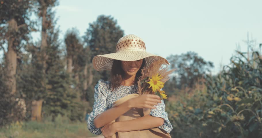 beautiful sweet sexy girl in a blue dress and hat walking on a field of sunflowers , cheerful woman sniffing flowers, countryside style, lifestyle 4K video shooting by handheld gimbal
