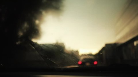 car on the road rain flows and wipers on the front windshield glass window of car with beautiful colorful blurry light of traffic outside street vehicle city raindrop travel weather slow motion