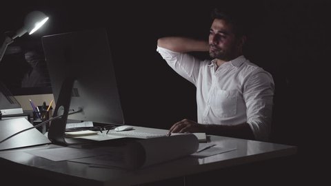 Workaholic Asian businessman working on computer late at night in the office feeling tired and having back pain from overwork