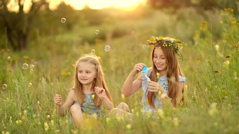 Little girls are blowing bubbles and laughing on the summer meadow with high grass