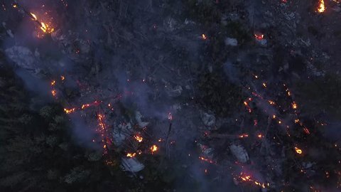 BC Wildfire burning and flames in overhead 4k drone shot. Aerial view onto forest fire at twilight or dawn. Flames, glow, blaze and smoke over dead woods and trees.