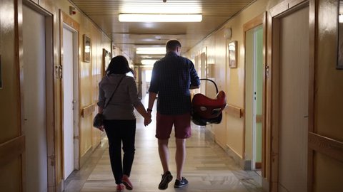 Parents with newborn baby in a car chair leavin the maternity hospital walk down the hall