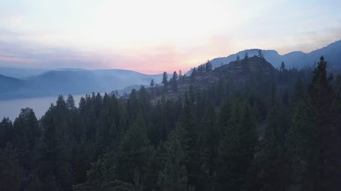 BC forest fire smoke covering mountains in 4k drone perspective. Rare view onto Okanagan landscapes affected by forest fire. Smoke covering trees, hills and lake. Sunset smoky skies