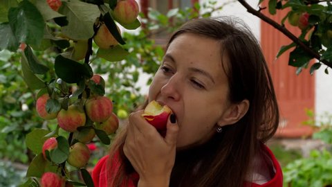 A girl eats a very appetizing apple with a garden tree