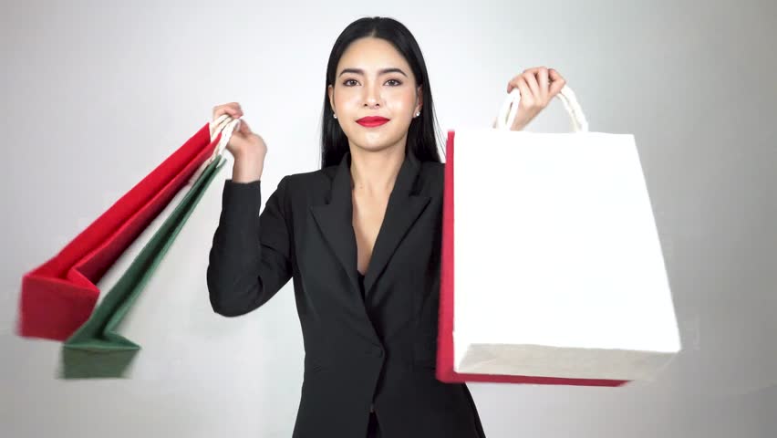 Young happy Asian woman holding a lot of shopping bags and turn around on white background