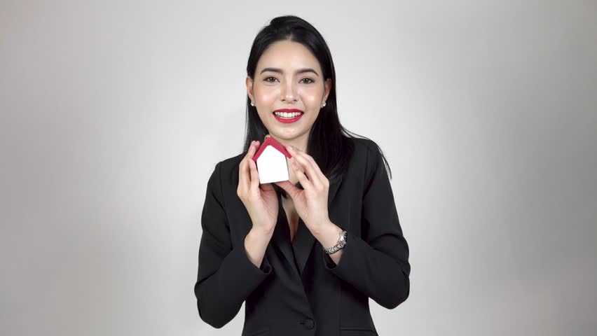 Young happy Asian woman holding a house toy and dancing on white background - Real estate and property concept