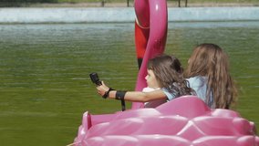 Children ride on a water attraction. Little girls ride on a water attraction with a motor. Sisters are riding a flamingo boat. Children with a video camera.