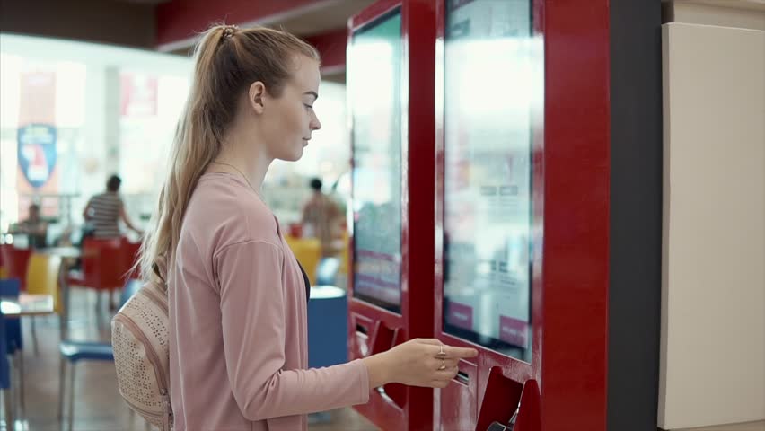 Young female visitor is making order in machine in hall of cafe with fast food. She is choosing meal on big display Royalty-Free Stock Footage #1015902775