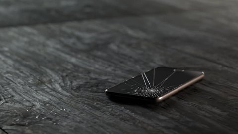 Smartphone crashes onto the wooden floor. Screen shatteres on impact. Slow motion shot.
