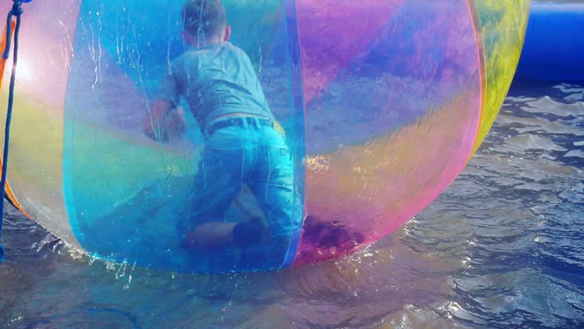 school age boy having fun in a large semi-transparent inflatable plastic ball that floats in water