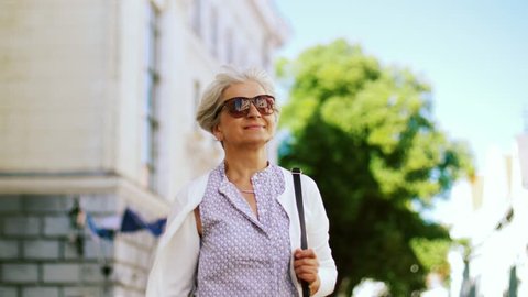 old age, retirement and people concept - happy senior woman walking along city street in summer