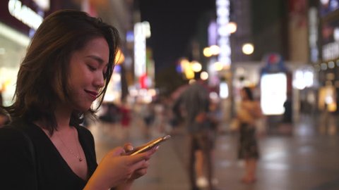 Side view of young asian woman using smartphone in the street at evening with slow motion, 4k
