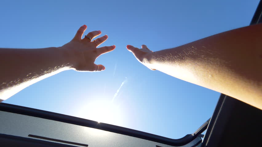 SLOW MOTION, CLOSE UP, POV, LENS FLARE: Cheerful woman with rings outstretching her arms through the sunroof of a car during her summer road trip. Carefree young female tourist enjoying a car cruise. Royalty-Free Stock Footage #1015927459
