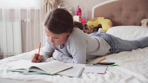 Little girl looks into book and writes in notebook on bed at home, steadicam shot Stock-video