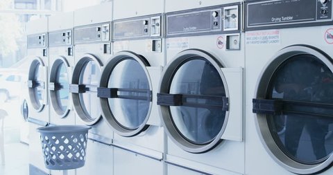 Woman putting clothes into washing machine at laundromat 4k
