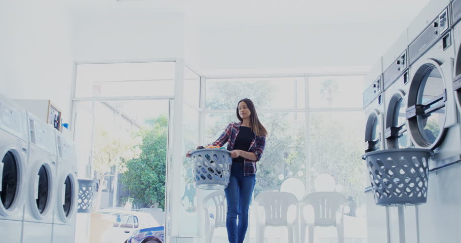 Beautiful woman carrying clothes in laundry basket at laundromat 4k
