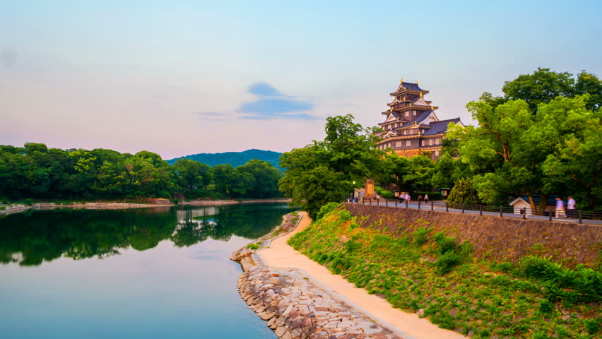 Okayama, Japan. Illuminated castle in Okayama, Japan at night with river and sunset colorful sky. Time-lapse at night from light to dark