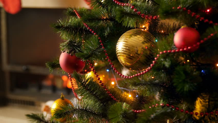 Closeup 4k video of beautiful golden and red baubles hanging on Christmas tree decoraetd with glowing colorful lights and garlands. Perfect background for winter celebrations and holidays | Shutterstock HD Video #1015934491