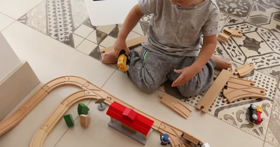 Two years old boy plays with wooden railroad in a sunny room