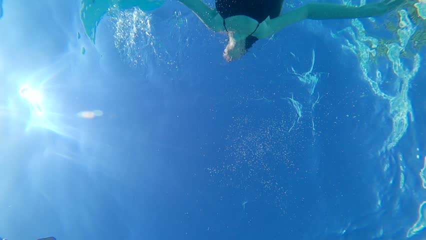 women with beautiful body into Swimsuit floating in clear blue water at pool in solar lighting, underwater bottom view
