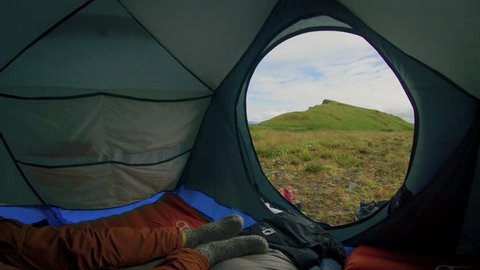 Young traveller or adventurer in camping adventure gear wakes up in tent, gets out of sleeping bag,walks outside to enjoy and breathe fresh air. Slow lifestyle outside city life in natural surrounding