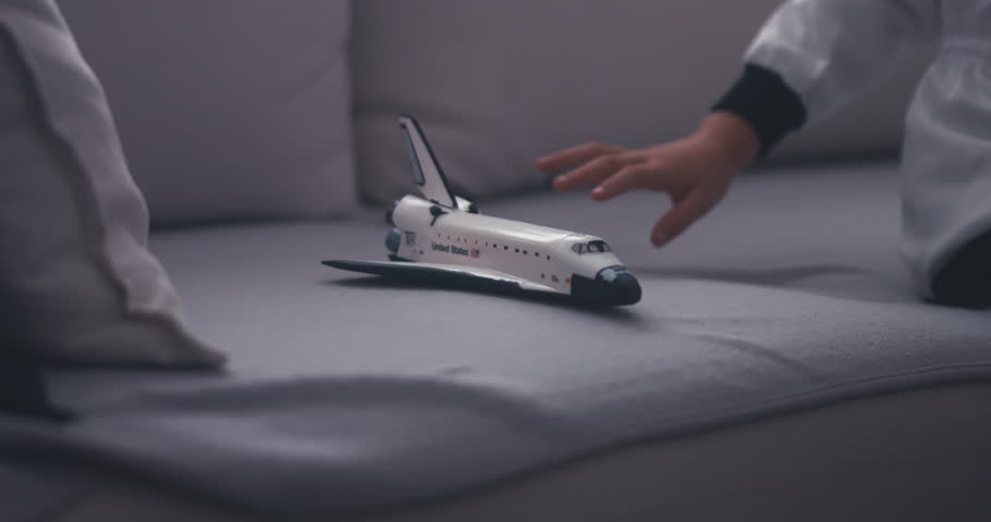 CU Cute little girl wearing astronaut suit playing with a toy space shuttle at home. Imagination concept. 4K UHD 60 FPS SLOW MO 