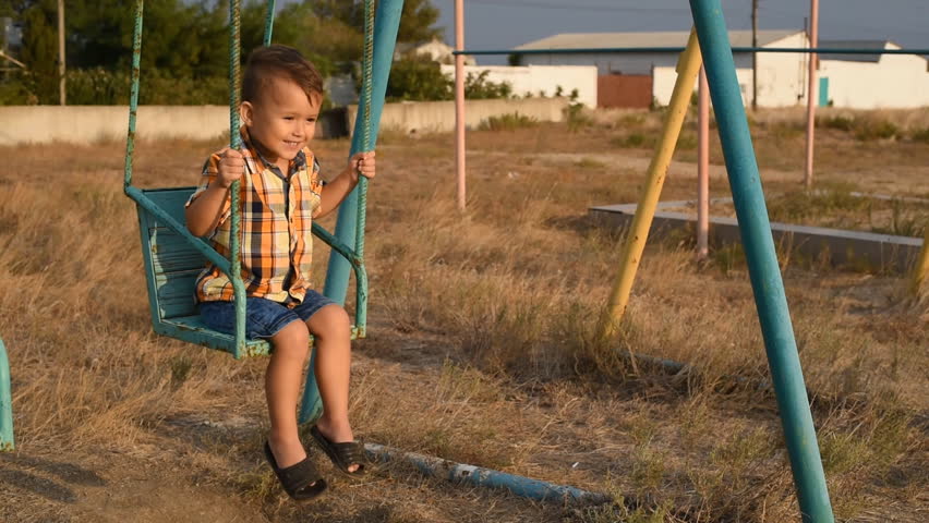 Baby on swing swinging one near the sea, in shirt and denim shorts