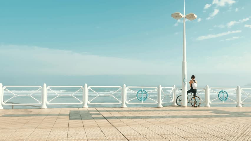 Young fitness girl on bicycle typing her smartphone at the morning Atalntic Ocean sealine, Cantabrian sea beach