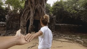 Follow me to concept, young woman leading boyfriend to ancient temple in Cambodia with tree roots on old ruins. Personal perspective of man holding hands following. People travel Slow motion
