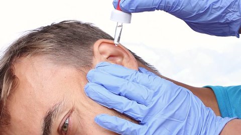 doctor in blue medical gloves with a pipette, drops a medicament in the ear of patient and massages the ear, closeup, white background