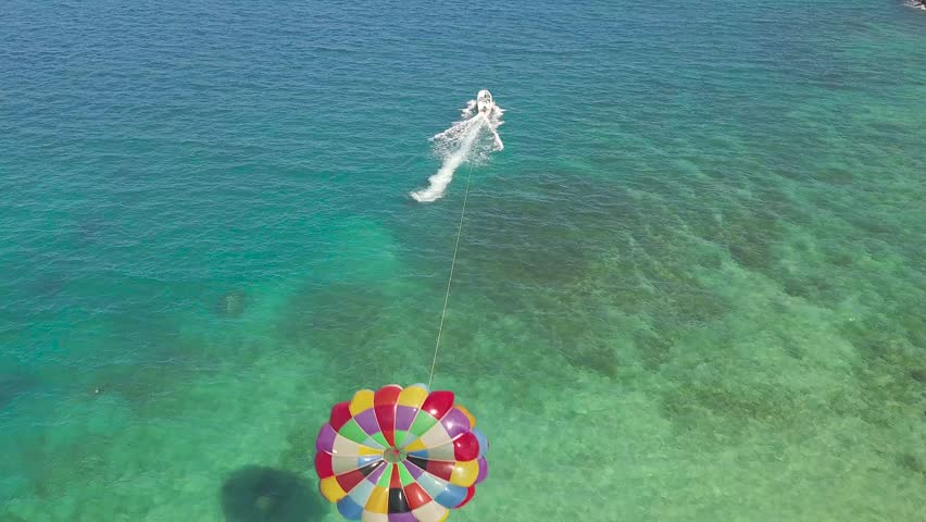 Parasailing in blue sea drone view. Aerial view parasailing in sea bay. Colorful parasail wing pulled by sailing boat in turquoise ocean water