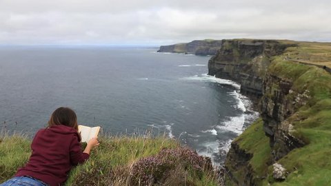 Girl reading a book at the Cliffs of Moher, Ireland