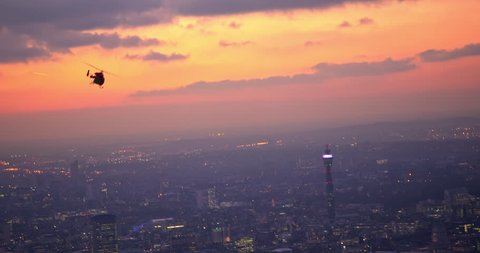 Stunning shot following London's rescue helicopter with beautiful sunset above London City. BT Tower, clouds, and city lights in the background.