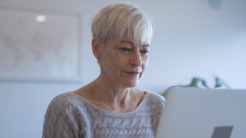 Dolly shot of senior woman using laptop computer while talking with man at home