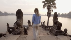 Shot of young woman on temples terrace by the lake at sunrise outstretching arms for happiness and freedom. People travel discovery concept 
Tourist female enjoying ancient temples of Asia exploring 