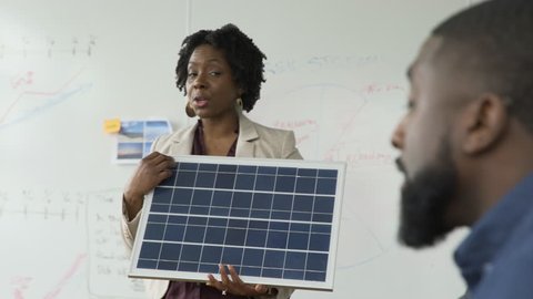 Handheld shot of businessman talking to colleague holding solar panel during meeting