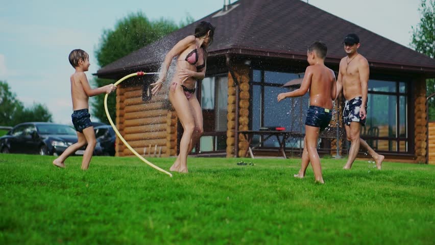 Family in the backyard of a country house in the summer relax playing with water and hosing
