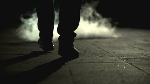 The legs of a man walking near the cloud of a smoke. slow motion