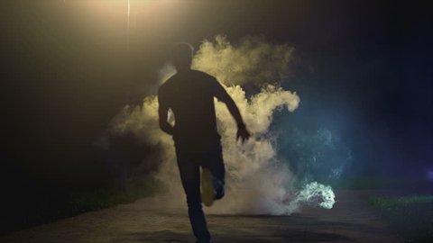 The man running in the cloud of smoke on the dark background, slow motion