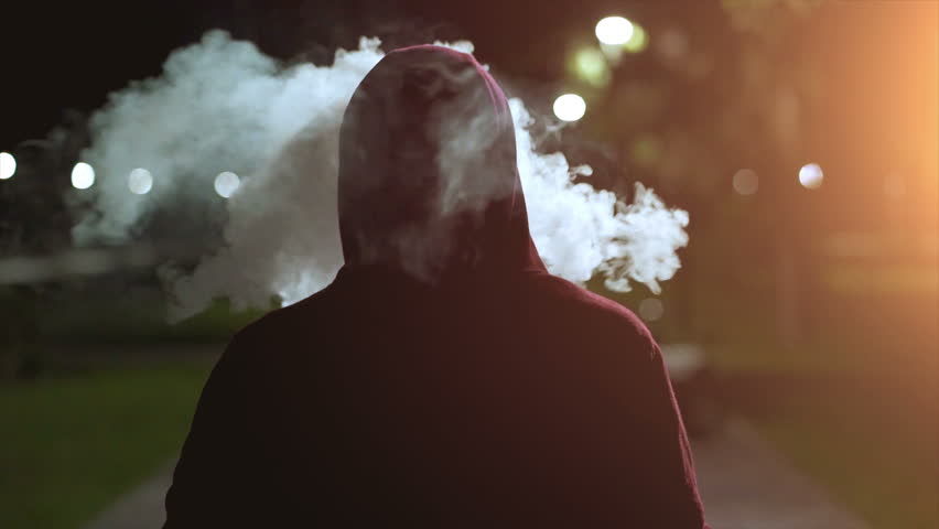 The fellow in a hood walking and smoking on the night street. slow motion