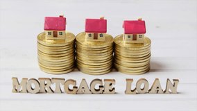 Conceptual footage of MORTGAGE LOAN words with golden coins and tiny model houses.